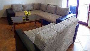 A living room with a sectional sofa, a coffee table with flowers, a painting on the wall, and an air conditioning unit. - Apartment with large garden to play football (Gajana)