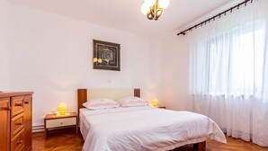 A bedroom with a wooden bed, white bedding, a nightstand with a lamp, a dresser, and a painting on the wall. - Apartment with large garden to play football (Gajana)