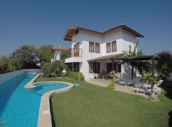 A two-story house with a swimming pool, a patio with outdoor furniture, and a garden.