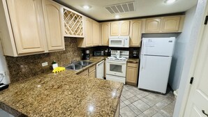 Una cocina con encimeras de granito, un refrigerador, un microondas, un horno, un lavamanos y armarios de madera.