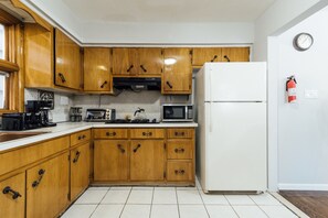 A kitchen with wooden cabinets, a white refrigerator, a microwave, a toaster, and a coffee maker. - 3 Bedroom near Journal Square (Jersey City)