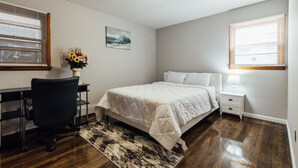 A bedroom with a bed, desk, chair, and a painting on the wall.