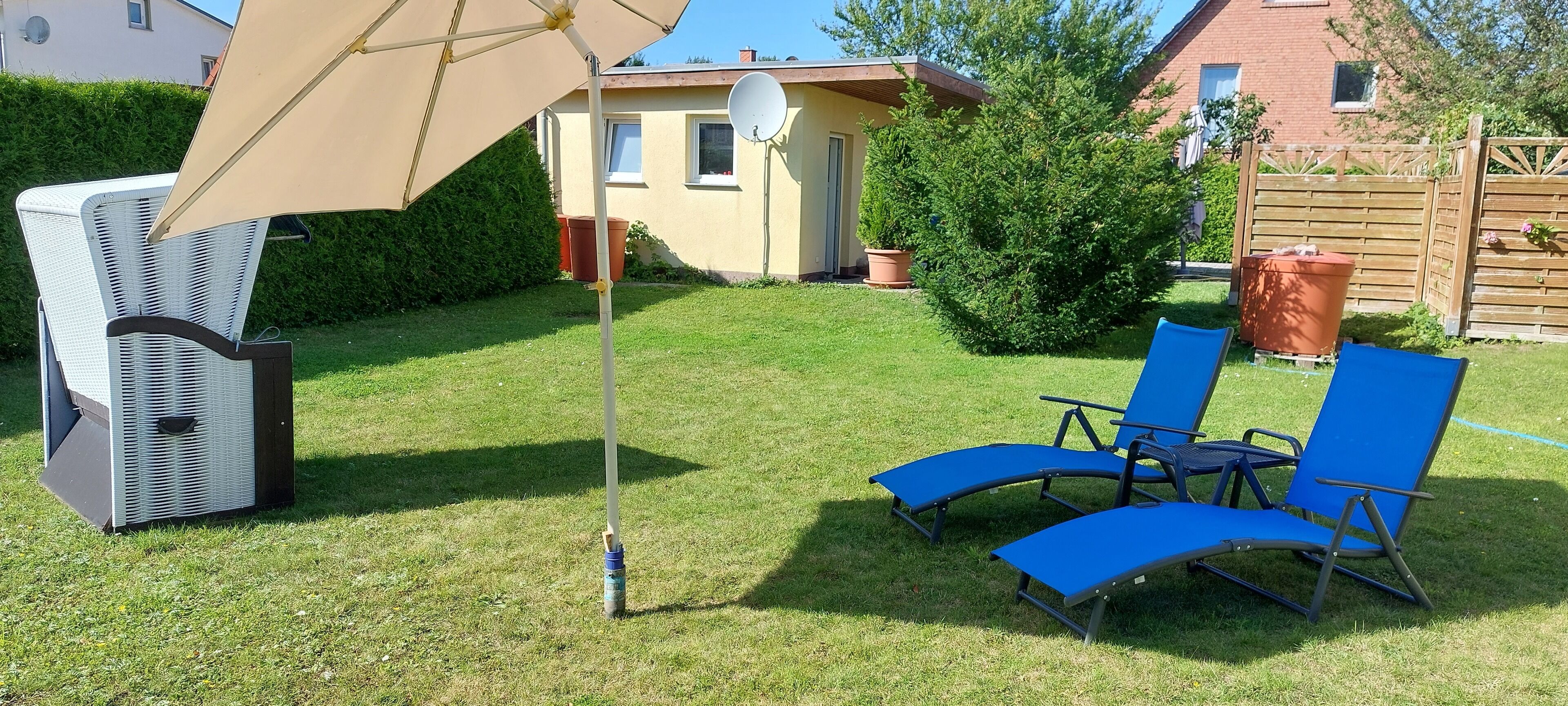 Un jardin avec un chauffage d’extérieur blanc, un parasol beige et deux chaises longues bleues.