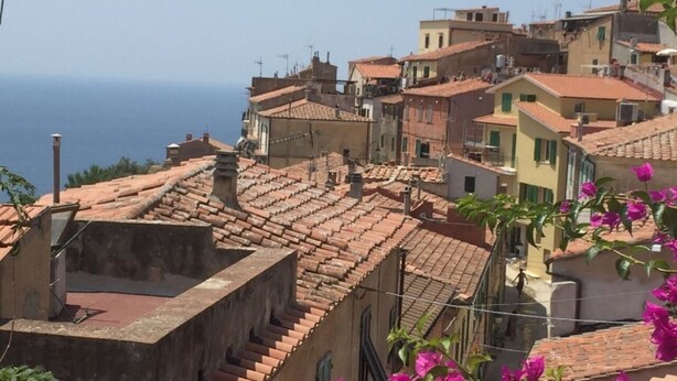 A coastal town with terracotta-roofed buildings, a clear view of the sea, and a person walking on a narrow street. - Il Rifugio - Capoliveri  - IL RIFUGIO (Capoliveri)