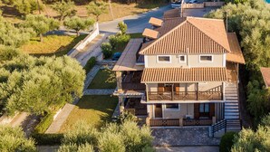 Un bâtiment à deux étages, doté d’un toit en tuiles, entouré de verdure et bordé par une route.