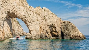 Un bateau naviguant à travers une arche naturelle formée par des rochers, au milieu d’une étendue d’eau.