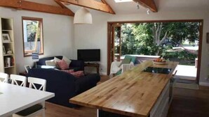 A cozy living area with a wooden dining table, a sofa, and a television. - Tui Cottages - House+Cottage - close to beach (Bundeena)