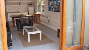 A compact living space with a kitchenette, a dining area with a table and chairs, and a small seating area with a sofa and a coffee table. - Tui Cottages - House+Cottage - close to beach (Bundeena)
