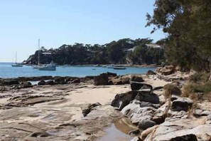 Una playa rocosa con barcos, árboles y un cielo despejado.