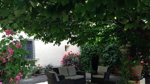 A covered outdoor seating area with wicker furniture, surrounded by lush greenery and flowering plants. - Authentic Tuscan Villa with Pool and Panoramic Views near Vinci – Tuscany (lamporecchio)