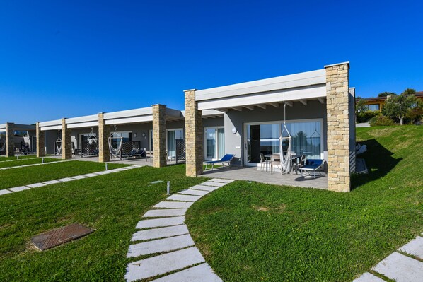 Ein modernes Hotel mit einer überdachten Außenbereich-Sitzgelegenheit, steinernen Säulen und blauem Himmel.