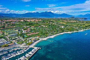 A coastal town with a marina, residential areas, and mountains in the background. - Relais Rosa dei Venti: 1 bedroom elegance, 2 pools, lake view! (Moniga del Garda)