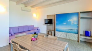 A modern room with a wooden dining table, purple sofa, TV, and a large window with a wooden deck view. - Relais Rosa dei Venti: 1 bedroom elegance, 2 pools, lake view! (Moniga del Garda)