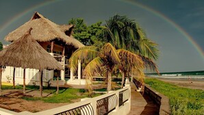 Ein Strandresort mit strohgedeckten Häusern, Palmen und einem sichtbaren Regenbogen.