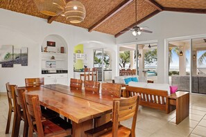 Un comedor amplio con una gran mesa y sillas de madera, una cocina con armarios blancos y vistas al océano a través de amplios ventanales.