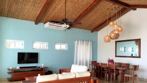 Ein Wohnzimmer mit einer Couch, einem Fernseher, einem Deckenventilator und einem Essbereich.