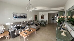 A living room with a grey sofa, a wooden coffee table, and a dining table with chairs. There is a painting on the wall and a chandelier hanging from the ceiling. - Fantastic penthouse of 140m2 (Torrox)