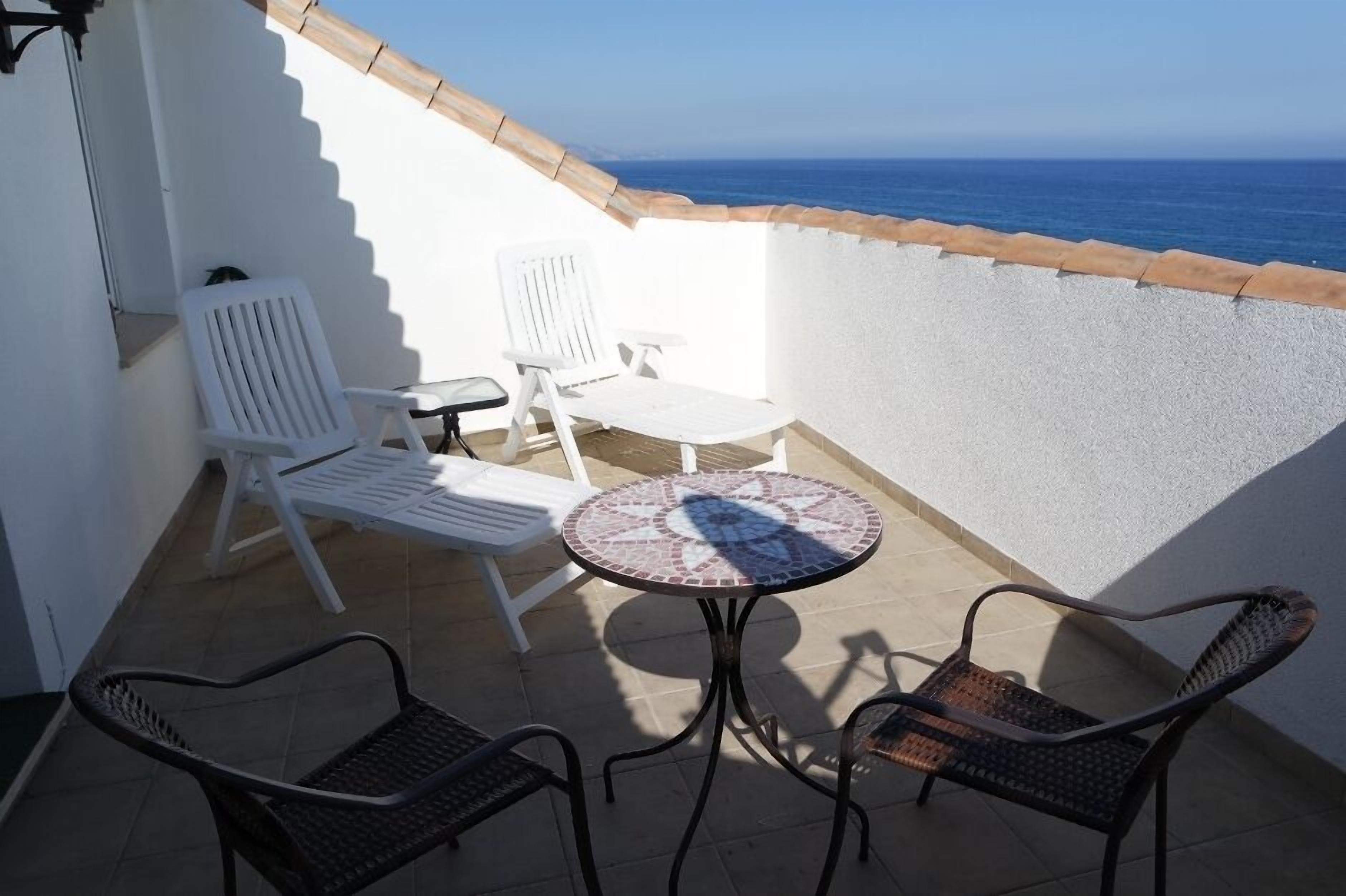 A balcony with white chairs, a small round table, and a view of the sea.