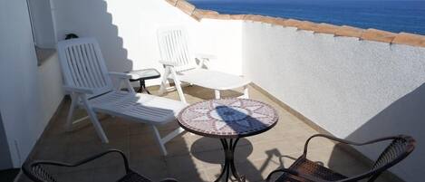 A balcony with white chairs, a small round table, and a view of the sea.