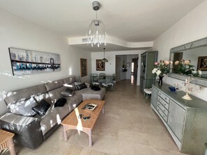 A modern living room with a grey sofa, a wooden coffee table, and a dining area with a green chair and a small table.