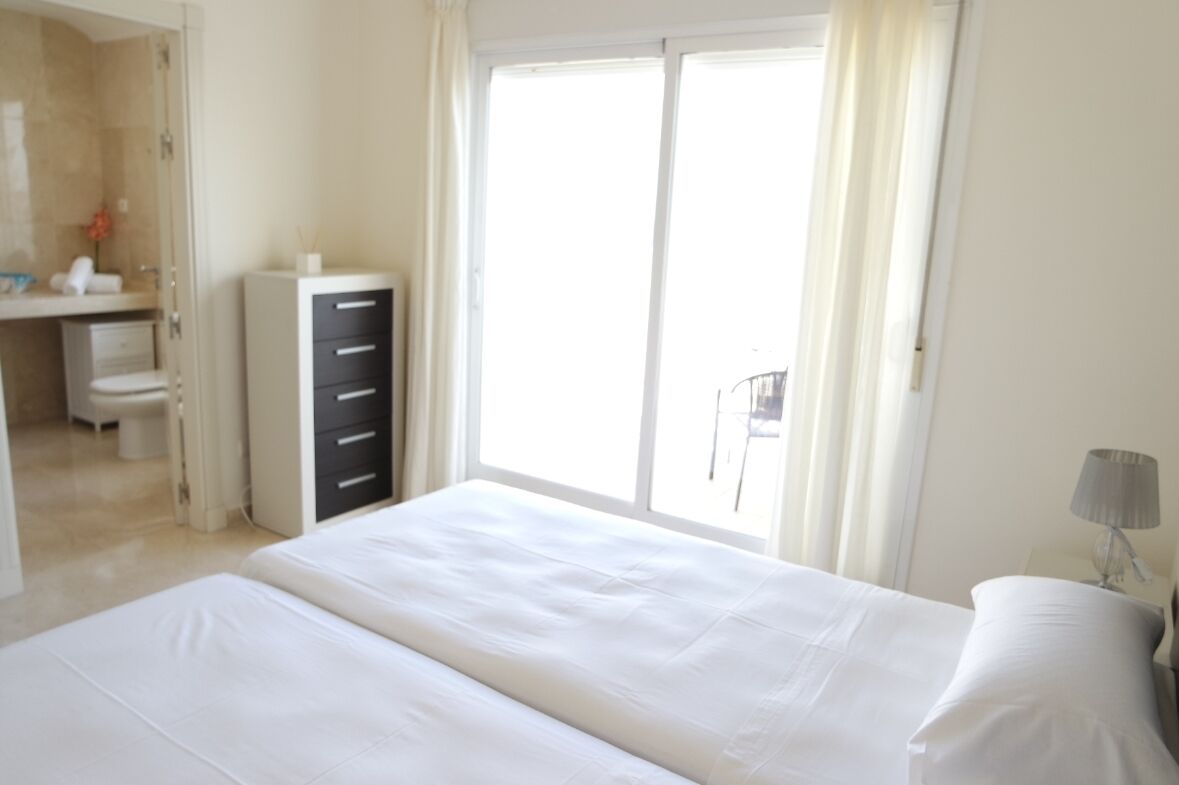 A hotel room with a large bed, a desk with drawers, a bathroom, and a balcony with curtains.