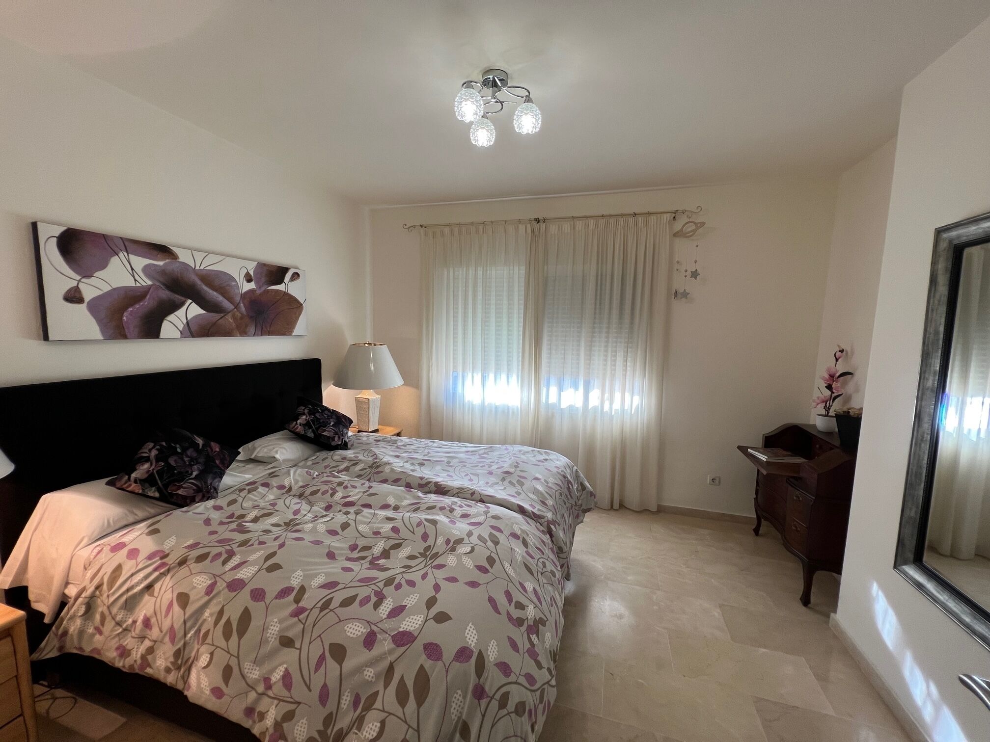 Un dormitorio con una cama grande, una mesita de noche con lámpara, un aparador y un espejo amplio.