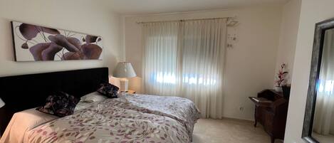 Un dormitorio con una cama grande, una mesita de noche con lámpara, un aparador y un espejo amplio.