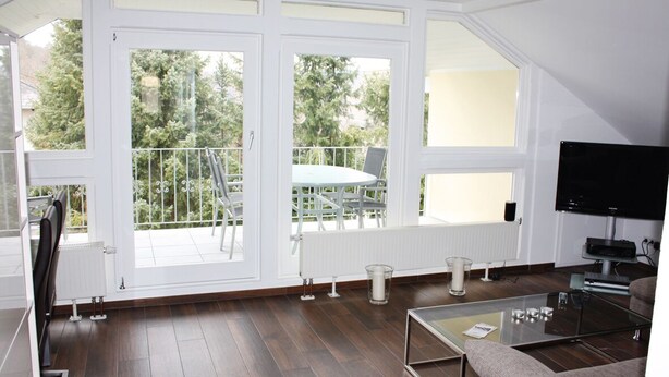 A modern living room with a glass coffee table, a sofa, a TV, and a balcony with a table and chairs.