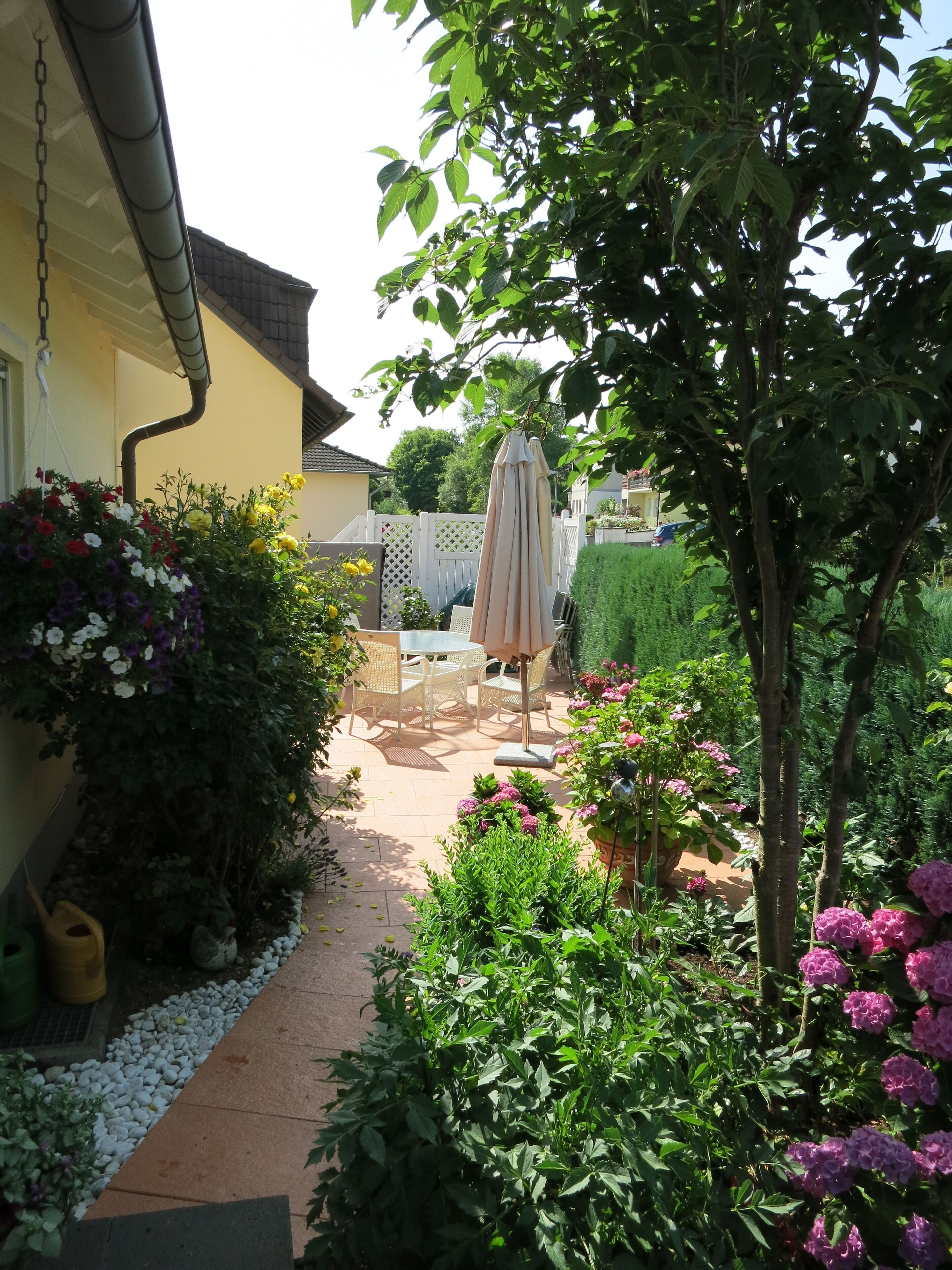 Ein Garten mit einer Terrasse, einem Hängesessel und einem Tisch mit Stühlen.