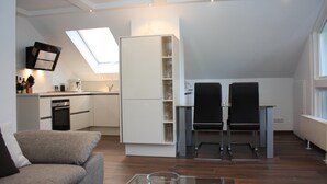 A modern apartment with a kitchen, dining area, and living space. It features a skylight, a built-in refrigerator, and a glass coffee table.