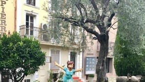 Une statue d’une femme, les bras tendus, dans un jardin où se trouvent plusieurs autruches.
