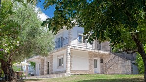 Ein zweistöckiges Steinhaus mit einem Balkon, einer überdachten Terrasse und einer Treppe, die zu dem oberen Stockwerk führt.
