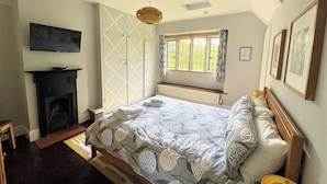 Un dormitorio con cama, chimenea, ventana con cortinas e iluminación en el techo.