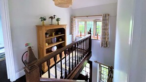 Una escalera con barandilla de madera que lleva a una zona de descanso con una consola de madera, plantas en macetas y una lámpara colgante.