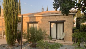 A stone building with a tiled roof, two windows with curtains, and a chair outside. - Villa Manzanillo w/ Private Pool, Sea Views, Double Badminton Court (pickleball) (Peyia)