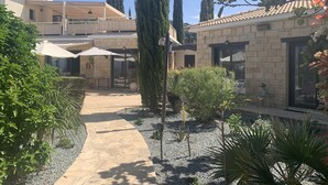A courtyard with a stone pathway, outdoor seating, and a variety of plants. - Villa Manzanillo w/ Private Pool, Sea Views, Double Badminton Court (pickleball) (Peyia)