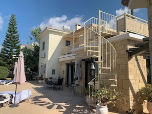 Un bâtiment à deux étages doté d’une façade en pierre, d’un balcon avec une rambarde en métal et d’un espace extérieur aménagé avec des parasols.
