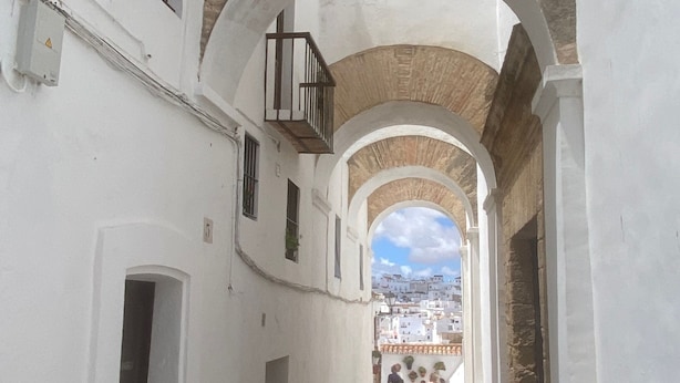 A narrow corridor with white walls and stone arches, leading to a view of a town. - Elegant Apartment in Vejer Old Town, renovated but with lovely original features (Vejer de la Frontera)