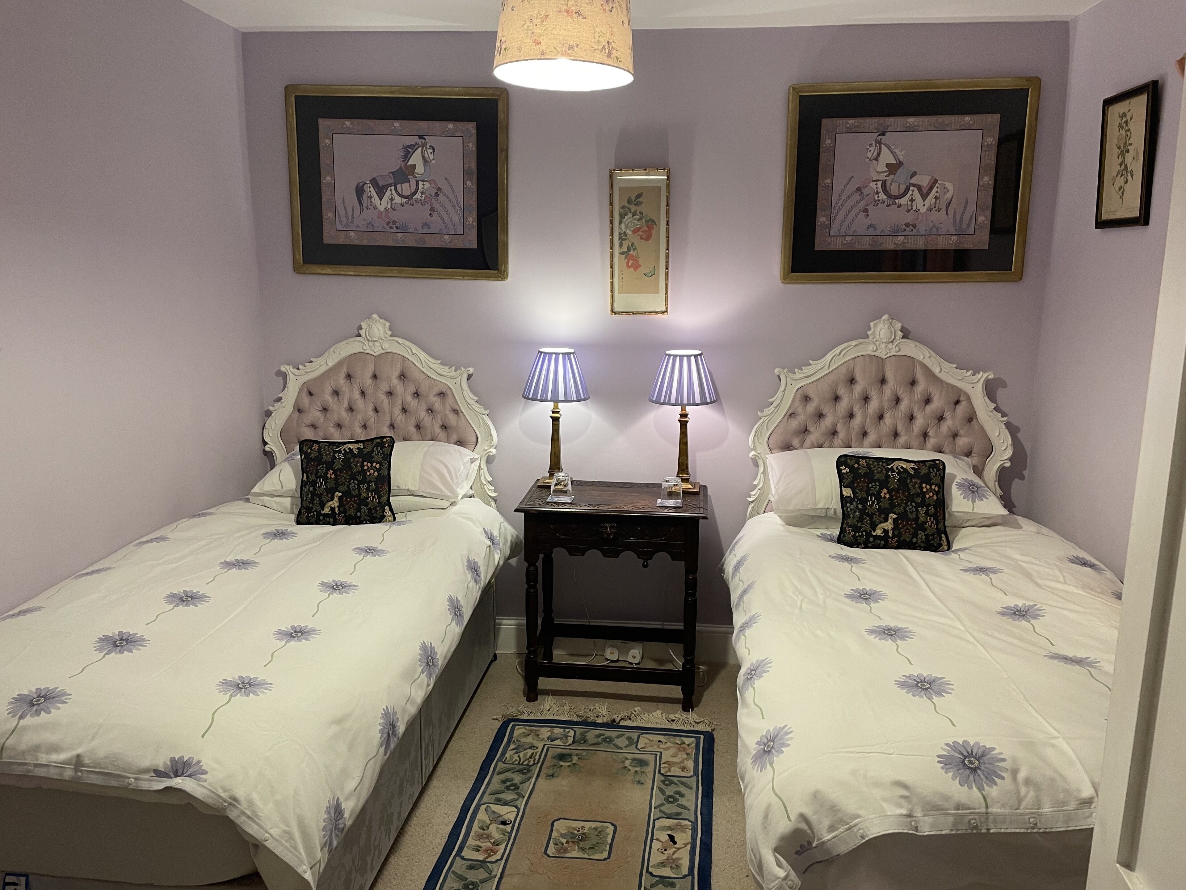 Ein Schlafzimmer mit zwei Betten, jeweils mit einem blumigen Überwurf und passenden Kissen, flankiert von Nachttischen mit Lampen.