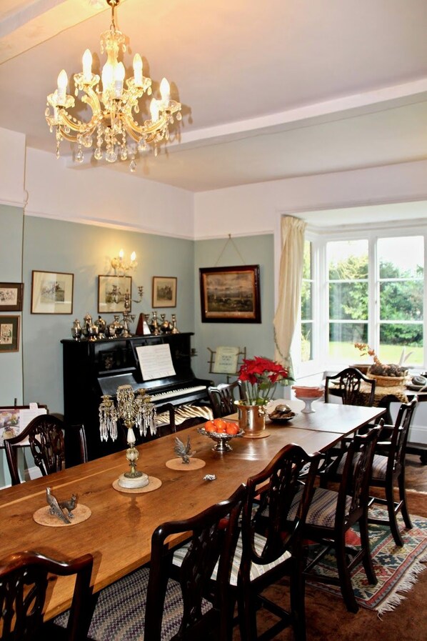 A dining room with a piano, wooden chairs, a chandelier, and framed pictures on the walls.