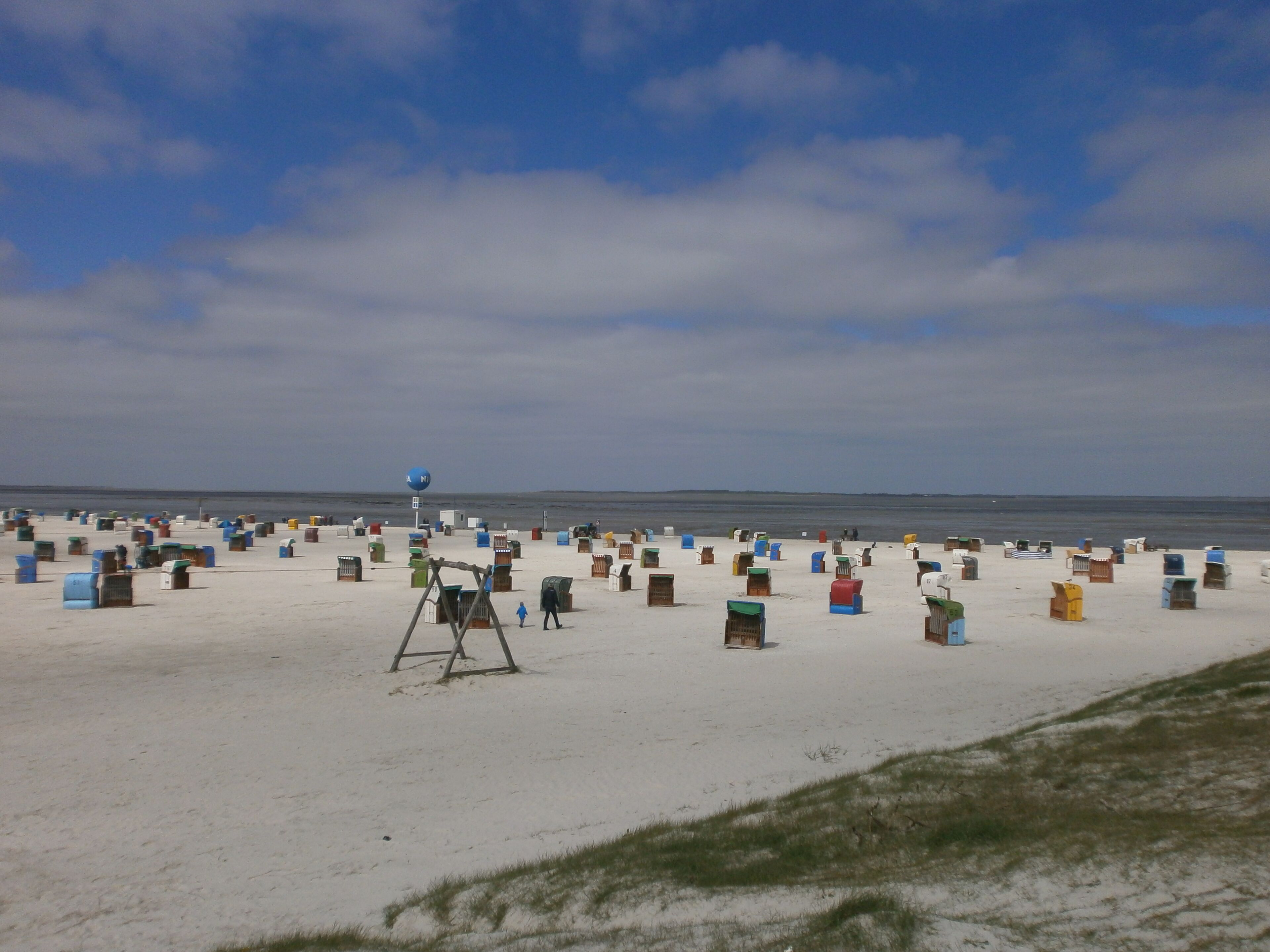 A beach with numerous colorful beach huts and a large blue sign with a compass.
