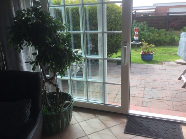 A room with a sliding glass door leading to an outdoor area with a garden and a blue planter. - Comfortable vacation home / close to the beach / quiet location - directly behind the dike (Dornumersiel)