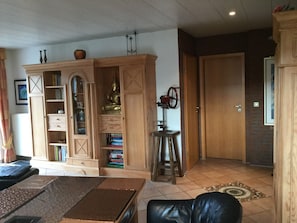 A living room with a wooden cabinet, a black leather sofa, and a patterned rug. - Comfortable vacation home / close to the beach / quiet location - directly behind the dike (Dornumersiel)