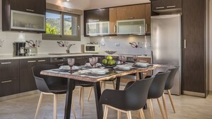 A modern kitchen with dark wood cabinets, stainless steel appliances, and a dining table set for six. - Sailing Villa Kefalonia (Karavados / Leivathos)