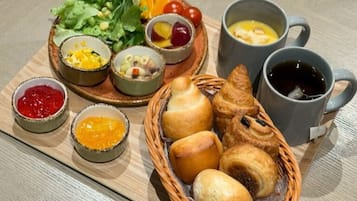 A breakfast tray with bread, pastries, fruit, and condiments.
