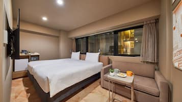 A hotel room with a bed, a small table with a plant, a sofa, and a window with curtains.
