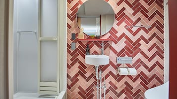 A bathroom with a herringbone patterned wall, a round mirror, a white sink, and a toilet paper holder.