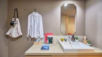 A modern bathroom with a white sink, mirror, and towel rack. There are toiletries on the counter and a book on the sink.