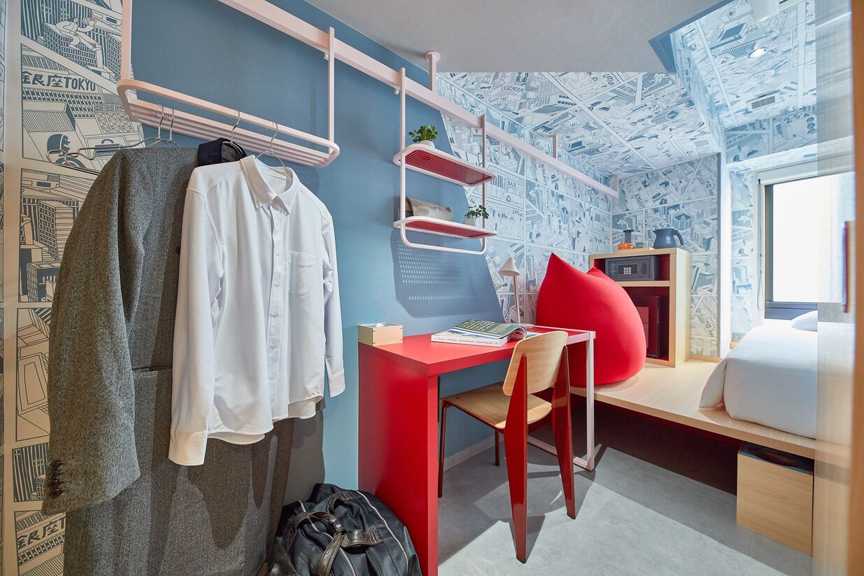 A room with a bed, a desk, a chair, a hanging rack, and a wall with a map pattern.