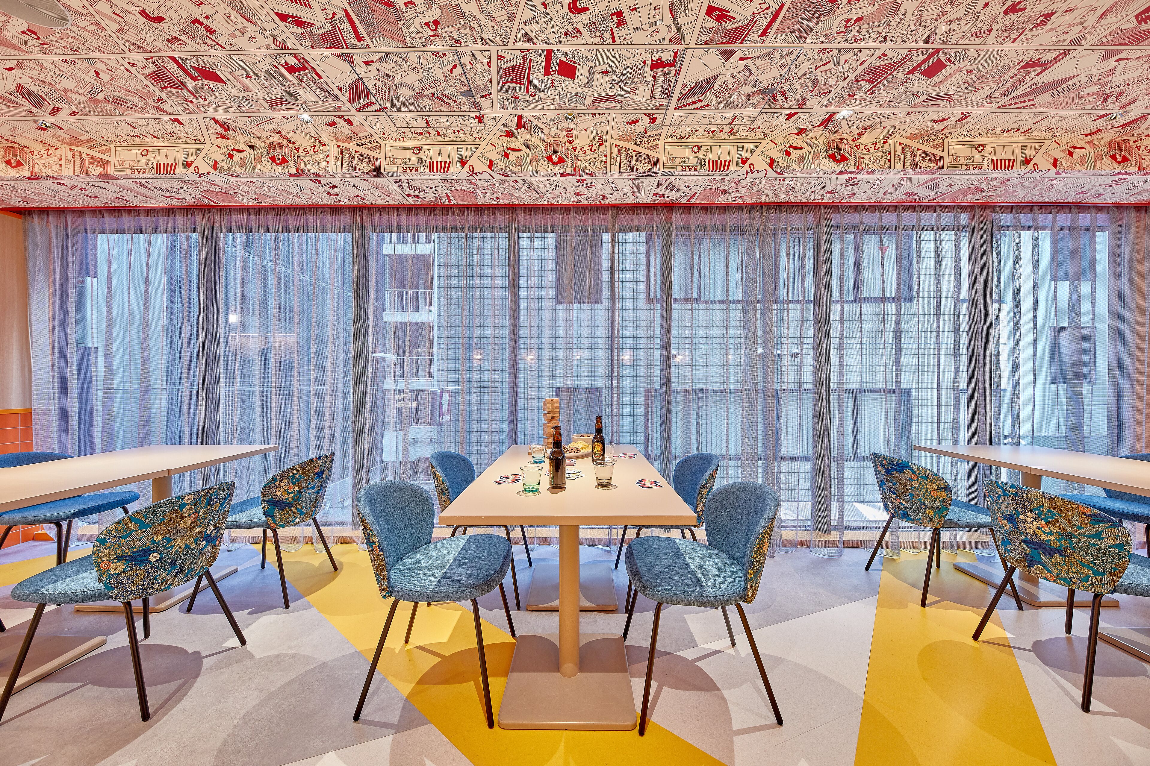 A modern conference room with a large table, blue patterned chairs, and a ceiling with a cityscape mural.